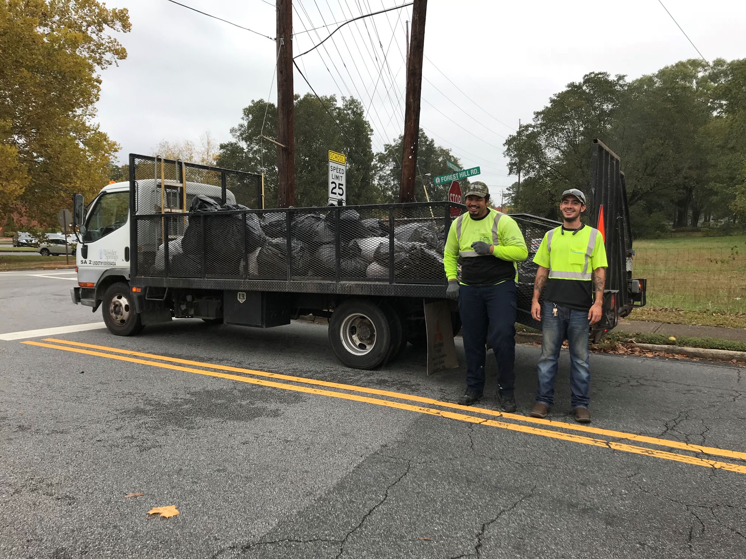 Two members of the Powder Springs sanitation department staff pose in front of a truck full of bags 