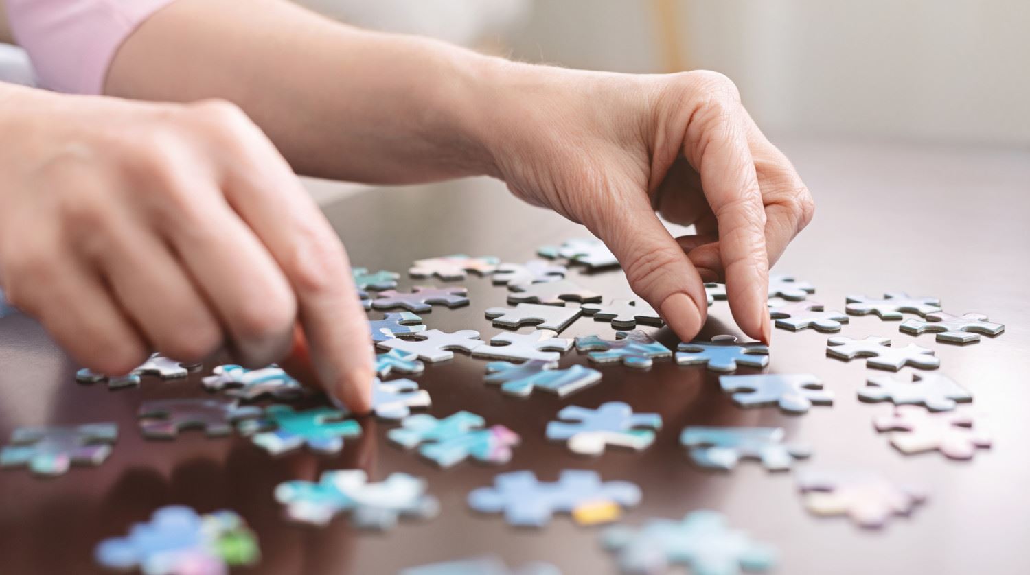 Hands putting together a jigsaw puzzle on a wooden table.