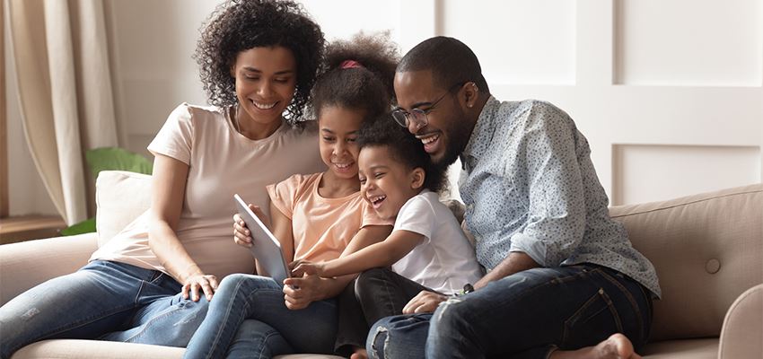 African American family of four gathered around a tablet watching a virtual tour.
